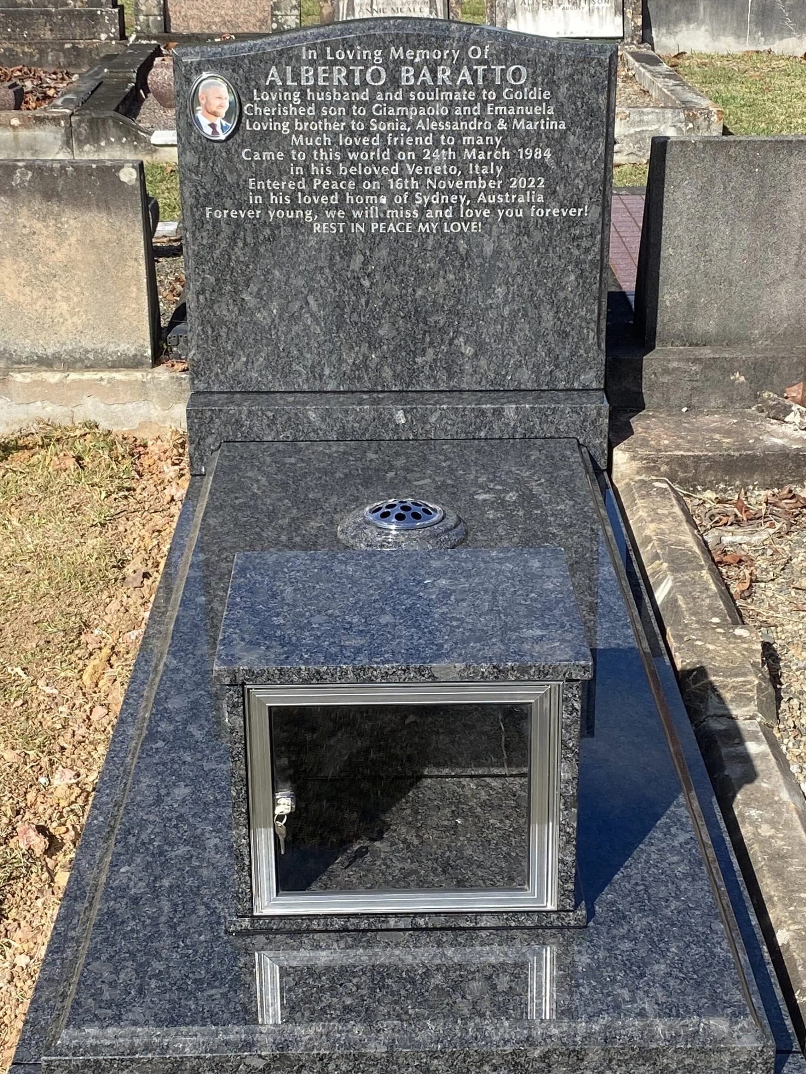 Single full Italian monument with a serpentine-shaped headstone, silver paint lettering, noble grey granite, and a candle box.